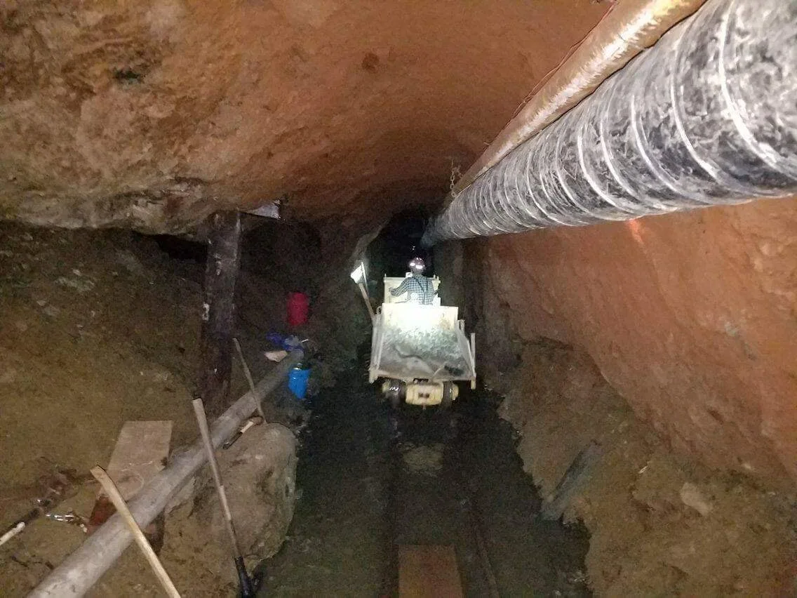 A narrow underground passage with mining equipment and ventilation.